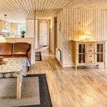 Wohnzimmer mit Holzwänden, Ledersofa und Holzboden. Durchgang zu Küche und Terrasse.