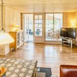 Wohnzimmer mit Holzwand, Fernseher und Sitzgelegenheiten. Durchgang zur Terrasse und Schlafzimmer.