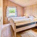 Schlafzimmer mit Holzwandverkleidung, Bett, Nachttisch und Fenstern.