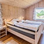 Schlafzimmer mit Holzwand, Bett, Nachttisch und zwei Fenstern.