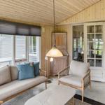 Wohnbereich mit Sofa, Sessel und Tisch. Holzwände und große Fenster.