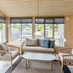 Wohnzimmer mit Holzwand, Sofa, zwei Sessel und Tisch. Große Fenster mit Blick nach draußen.