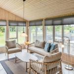 Wohnraum mit Holzwänden, Sitzgruppe und großen Fenstern zum Garten.