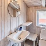 Badezimmer mit Waschbecken, Spiegel und Toilette. Holzwände und kleines Fenster.