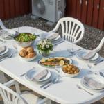 Weiße Terrassentisch mit Stühlen, gedeckt für sechs Personen mit Speisen und Getränken.