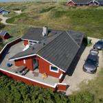 Rotes Ferienhaus mit Garage und Terrasse auf grüner Hügellandschaft.