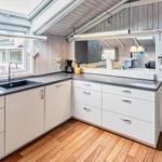 Küche mit Arbeitsfläche, Spüle und Fenster. Blick in Wohnbereich mit Sofa und Kühlschrank.