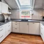 Küche mit weißen Schränken, dunklem Arbeitsplatz und Holzboden unter Dachschrägen.