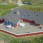Rotes Ferienhaus mit Terrasse und Garten, umgeben von Gras und Bäumen.