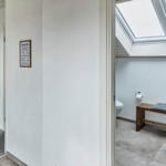 Badezimmer mit Dachfenster und Holzbank. Flur mit Spiegel und Blumen.