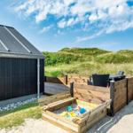 Holzterrasse mit Sitzgelegenheit und Sandkasten neben einem Haus mit dunkler Fassade.