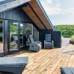 Terrasse mit Liegen und Sitzgelegenheiten. Holzdeck und Glaswände. Grill und Gartenzaun.