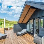 Terrasse mit Liegen und Sitzgelegenheiten vor modernem Haus mit Holzverkleidung und Glasfront.
