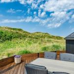 Terrasse mit Tisch, Stühlen und Blick auf grüne Dünen.