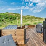 Terrasse mit Tisch, Stühlen und Blick auf grüne Dünen.