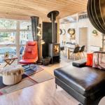 Wohnzimmer mit Sofa, roten Sesseln und Kamin. Holzwände und große Fenster.