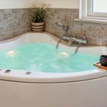 Eine Badewanne mit Whirlpool, gefüllt mit Wasser, daneben ein Holzbrett mit Tassen und Kerzen.