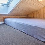 Schlafzimmer mit Dachschräge, Holzwänden und Dachfenster. Bett mit grauer Bettwäsche.