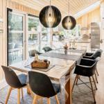 Essbereich mit Tisch, Stühlen und Kaminofen. Küche im Hintergrund. Holzwände und Boden.