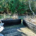 Terrasse mit Holzbank, Sitzgelegenheit und Pflanzenbeeten im Wald.