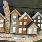 Holzfiguren von Häusern auf einem Ast, mit dem Schriftzug GODSET.