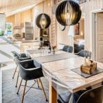 Essbereich mit Tisch und Stühlen, Küche im Hintergrund, Holzwände und moderne Beleuchtung.