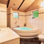 Bad mit Whirlpool, Waschbecken und Toilette. Holzdecke und Fenster mit grünem Glas.