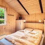 Schlafzimmer mit Holzwand, Bett, Fenster und Kleiderhaken.