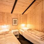 Zwei Betten in einem holzverkleideten Zimmer mit Fenster und Nachttisch.