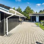 Pflasterweg führt zu einem Haus mit dunkler Holzfassade und Garten.