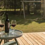 Auf der Terrasse steht ein Tisch mit Wein und einer Pflanze. Im Hintergrund ist ein Spielplatz mit Rutsche.