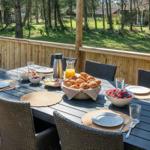 Terrasse mit Esstisch, Stühlen und Frühstückszubehör im Freien.
