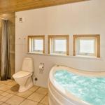 Bad mit Whirlpool, Toilette und Dusche mit Holzdecke und Fenstern.