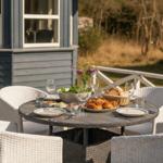 Rundtisch mit Stühlen und Speisen auf einer Terrasse vor einem Haus.