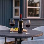 Runder Tisch mit Wein, Käse und Trauben auf Terrasse vor Haus.