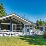 Ein Haus mit Terrasse, Grill und Garten. Im Hintergrund sind Bäume und ein kleines Nebengebäude zu sehen.