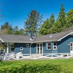 Ein blaues Ferienhaus mit weißem Geländer und Terrasse unter Bäumen.