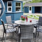Terrasse mit Tisch und Stühlen vor blauem Haus. Hinterhof mit weißem Zaun und kleinem Schuppen.