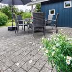 Terrasse mit Sitzgruppe, Sonnenschutz und Blumenbeet vor blauem Haus.