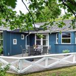 Blauer Holzhaus mit Terrasse und Garten. Tisch, Stühle und Sonnenschirm sind draußen.