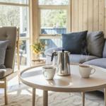 Runde Tisch mit Kaffeetasse und Kanne vor Sofa und Sessel.