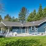 Blauer Ferienhaus mit Terrasse und Garten. Umgeben von Bäumen und Gras.
