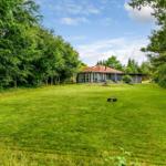 Haus mit rotem Dach und großem Garten zwischen Bäumen.