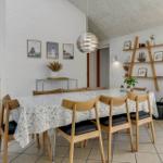 Esszimmer mit Holzstühlen, Tischdecke und Kaminofen. Wandregal und Bilder an der Wand.