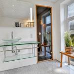Badezimmer mit Glaswaschbecken, Spiegel und Pflanze vor Fenster
