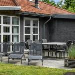 Terrasse mit Tisch, Stühlen und Liegestühlen vor einem Haus mit grauer Wand und rotem Dach.