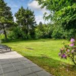 Terrasse mit Liegestühlen, grüner Rasen und blühenden Sträuchern im Hintergrund.