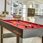Pooltisch mit Kugeln und Stöcken im Wohnbereich mit Fenstern und Küchenzeile.