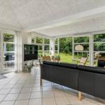 Wohnzimmer mit schwarzer Ledercouch, großen Fenstern und Blick auf Garten