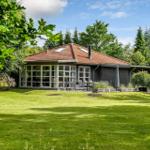 Haus mit rotem Dach, großem Glasbereich und Garten mit Liegestühlen.